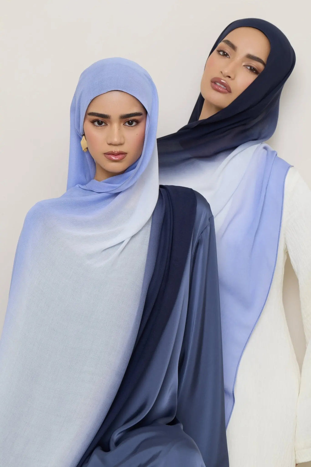Two women wearing light blue hijabs against a white background