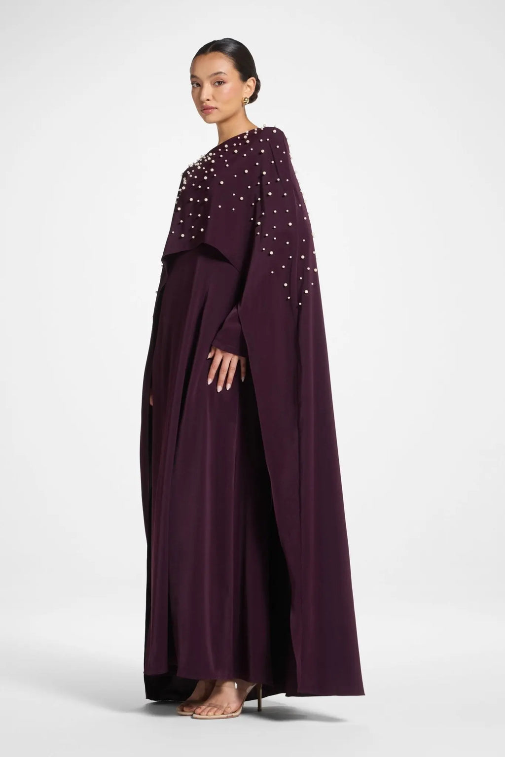 Woman wearing a long, dark purple dress with embellishments on a white background