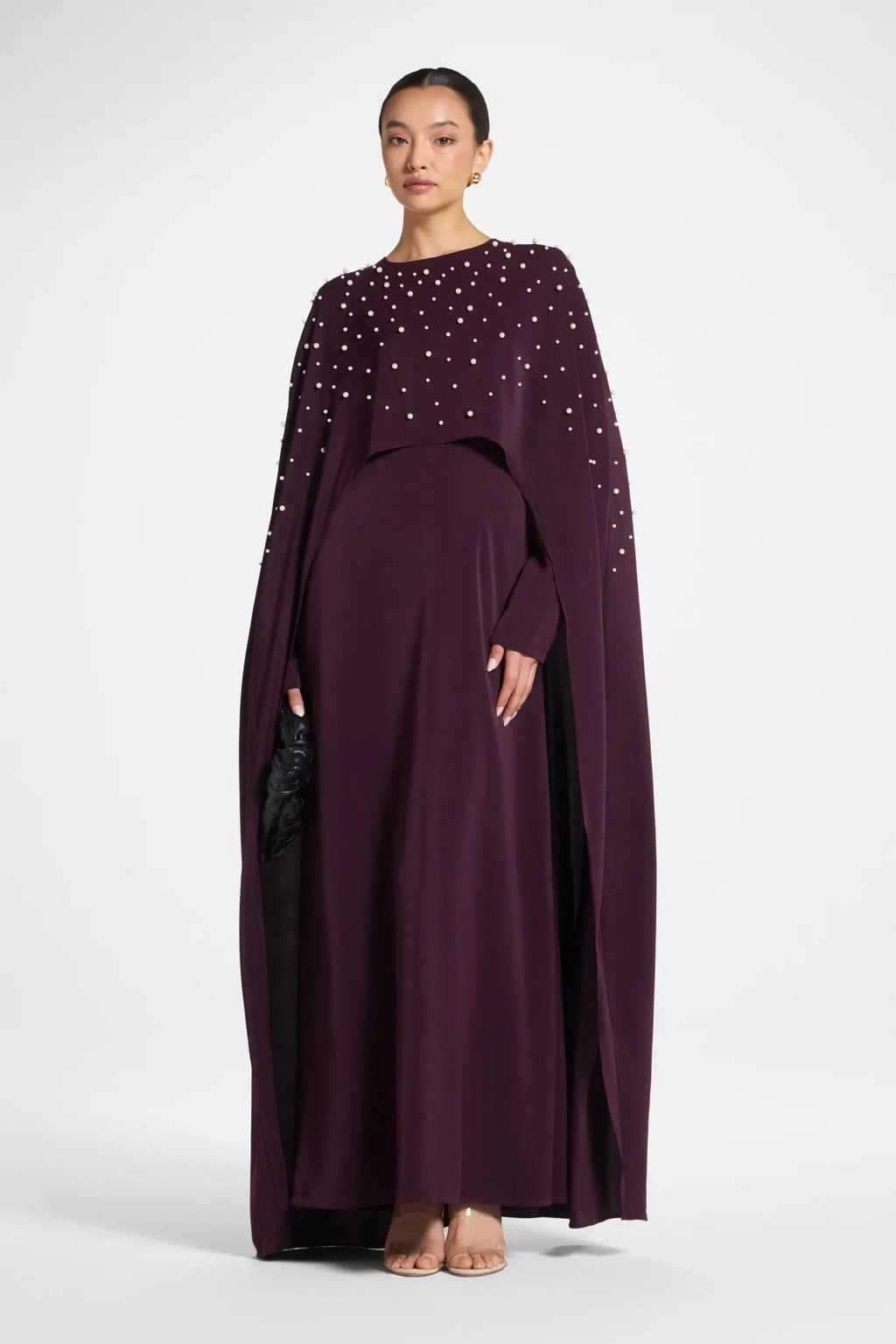 Woman wearing a long, dark purple dress with embellishments on a white background
