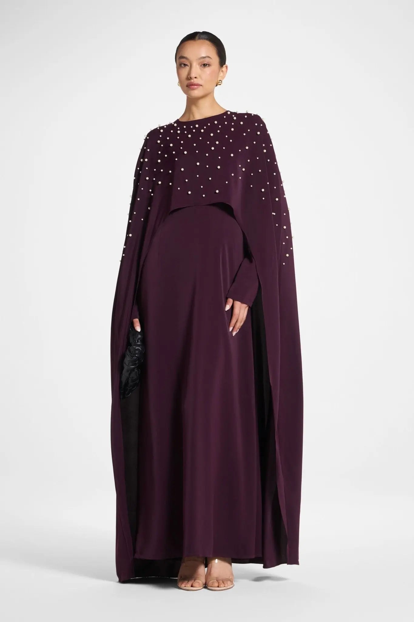 Woman wearing a long, dark purple dress with embellishments on a white background