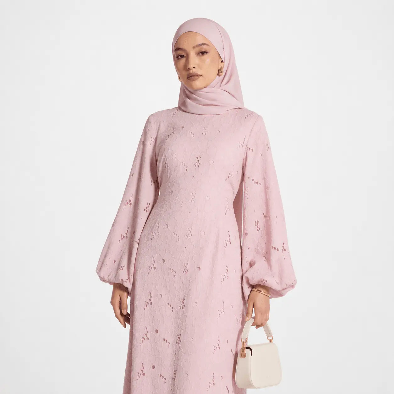 Pink lace modest dress with bell sleeves, matching hijab, and white handbag for elegant Muslim fashion