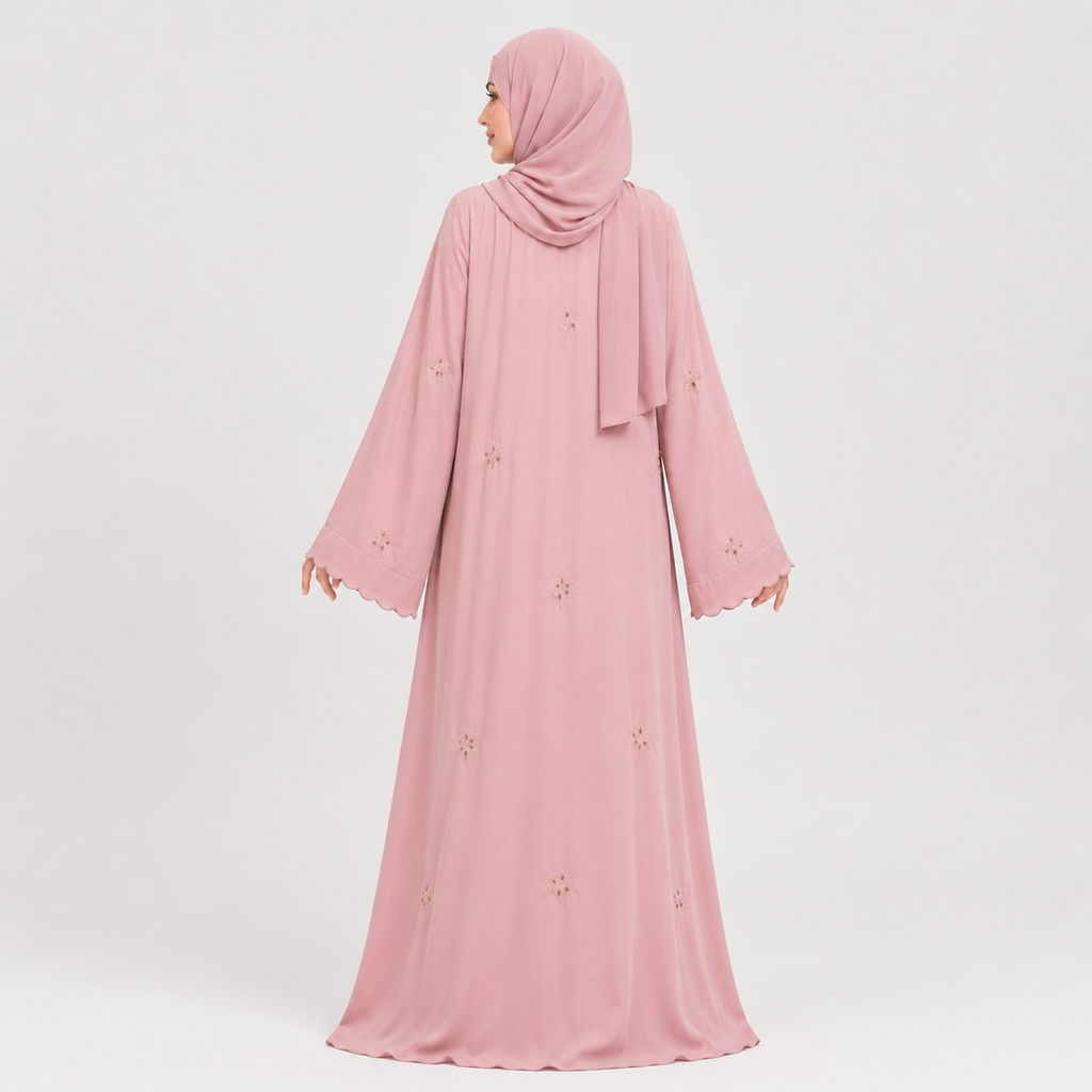 A woman wearing a long pink abaya dress with a matching hijab, shown from the back against a light gray studio background. The dress has long sleeves, a modest silhouette, and small embroidered floral details scattered across the fabric.