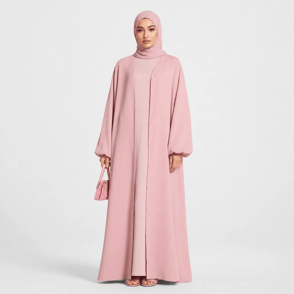 Woman wearing a pink abaya and hijab on a white background