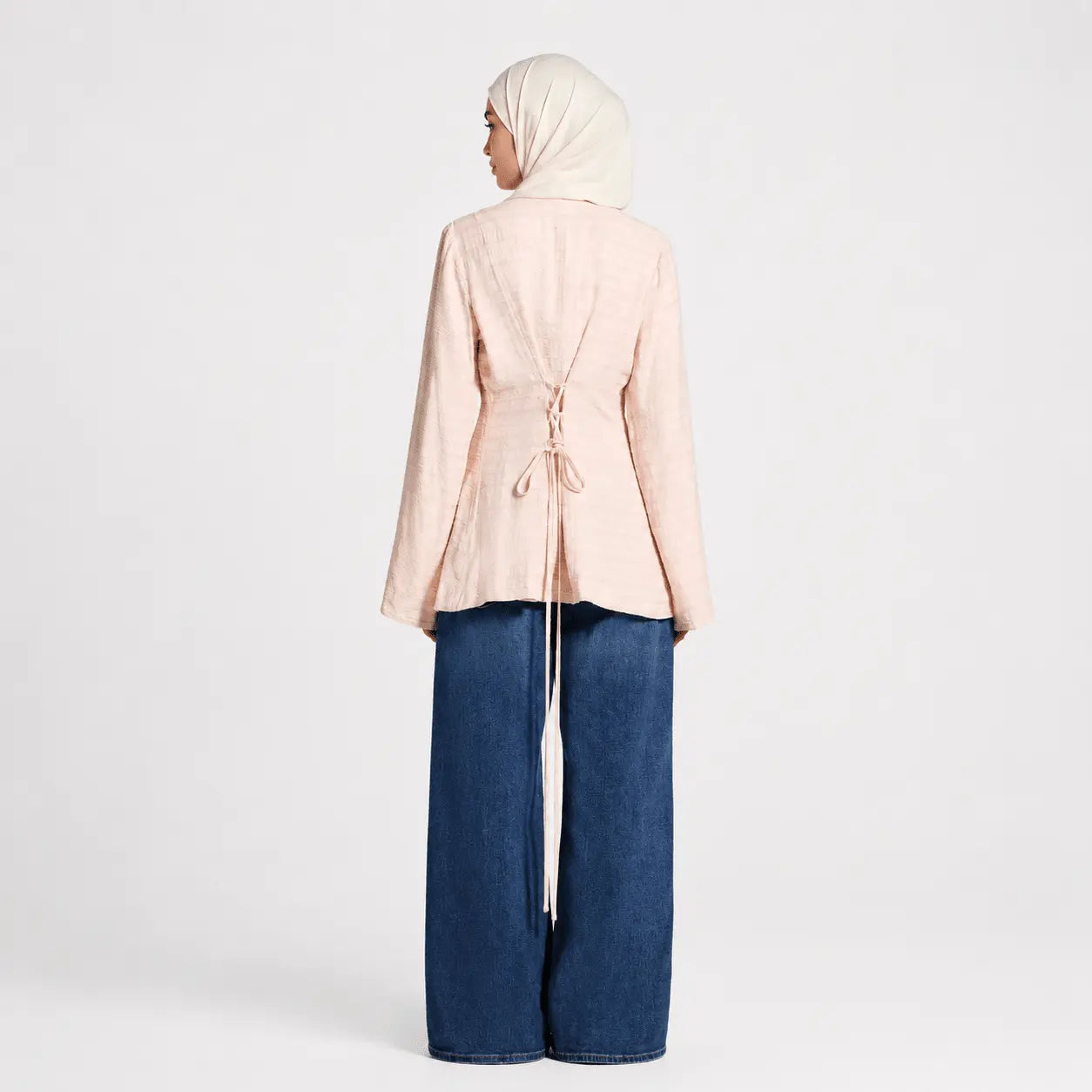 Person wearing a light pink top and blue jeans on a white background