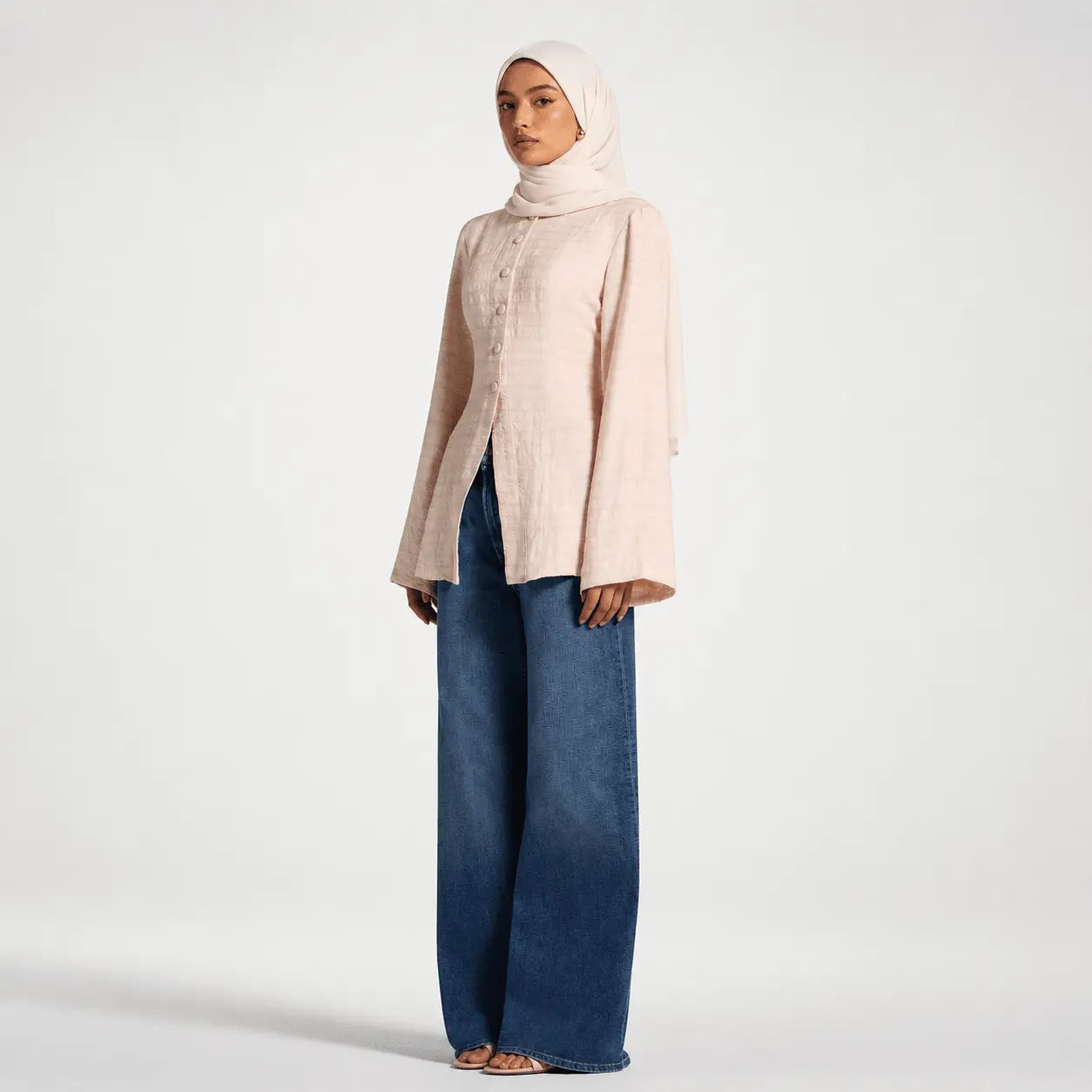 Woman wearing a light pink top and blue jeans on a white background