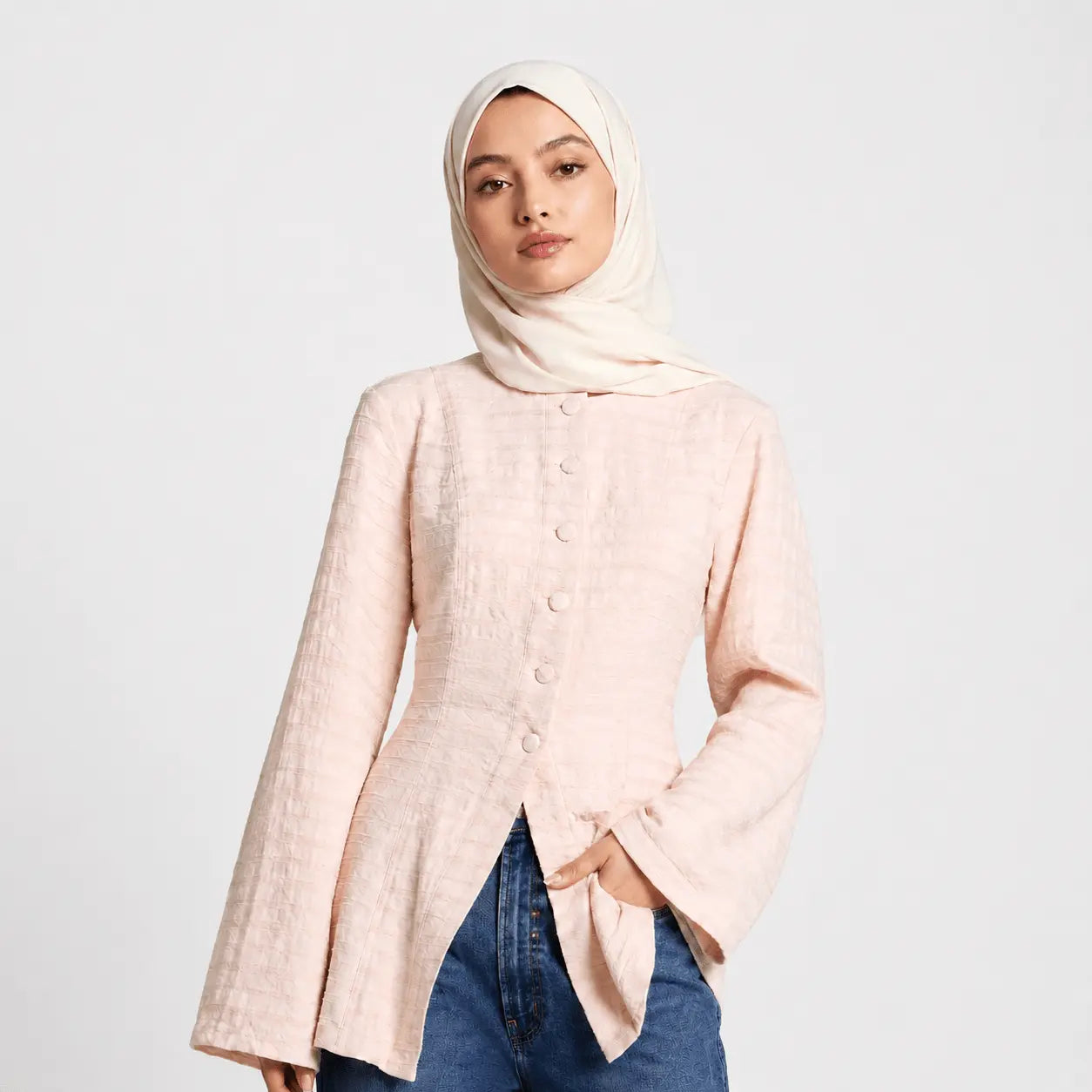 Woman wearing a light pink button-up shirt and blue jeans on a white background