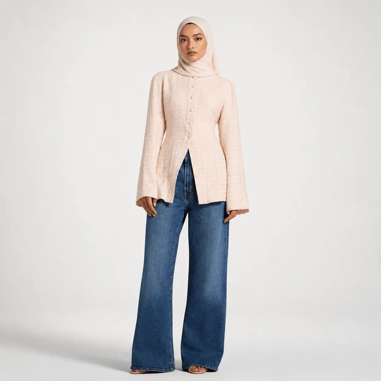 Person wearing a light pink blazer and blue jeans on a white background