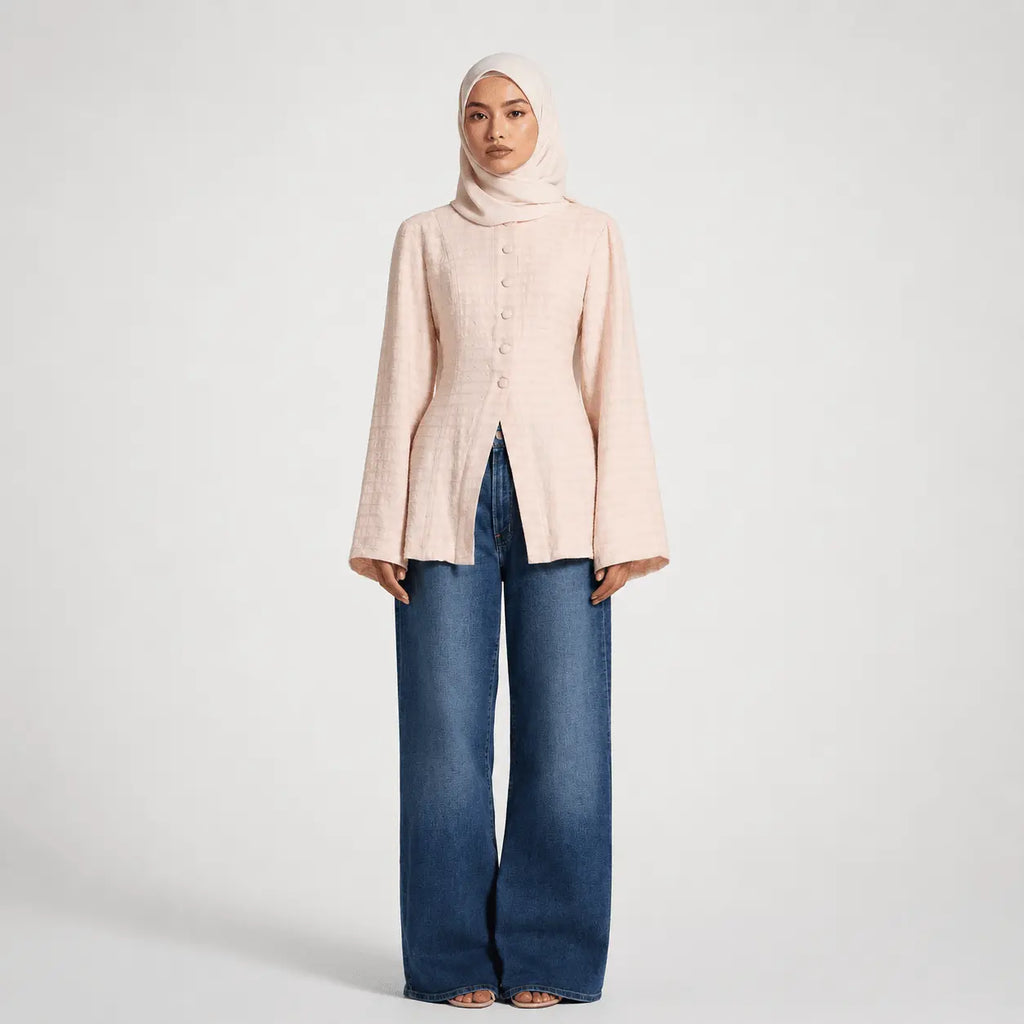 Woman wearing a light pink button-up shirt and blue jeans on a white background