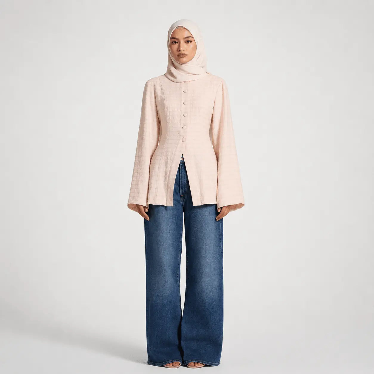 Woman wearing a light pink button-up shirt and blue jeans on a white background