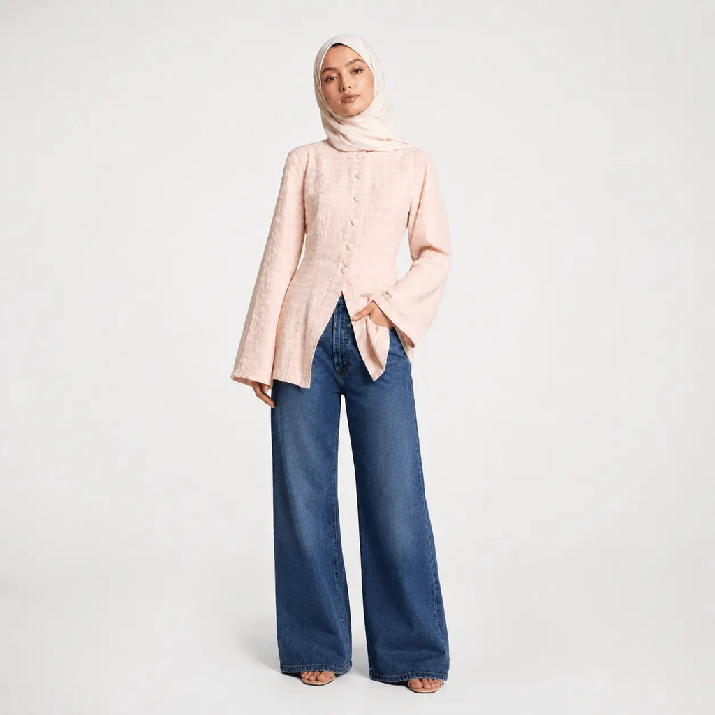 Woman wearing a light pink blouse and blue jeans on a white background