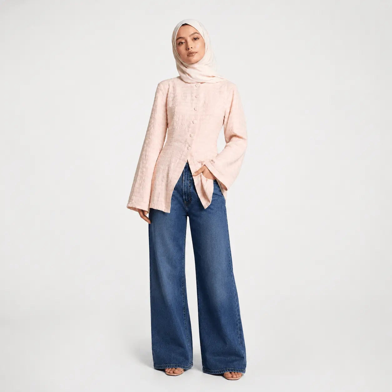 Woman wearing a light pink blouse and blue jeans on a white background