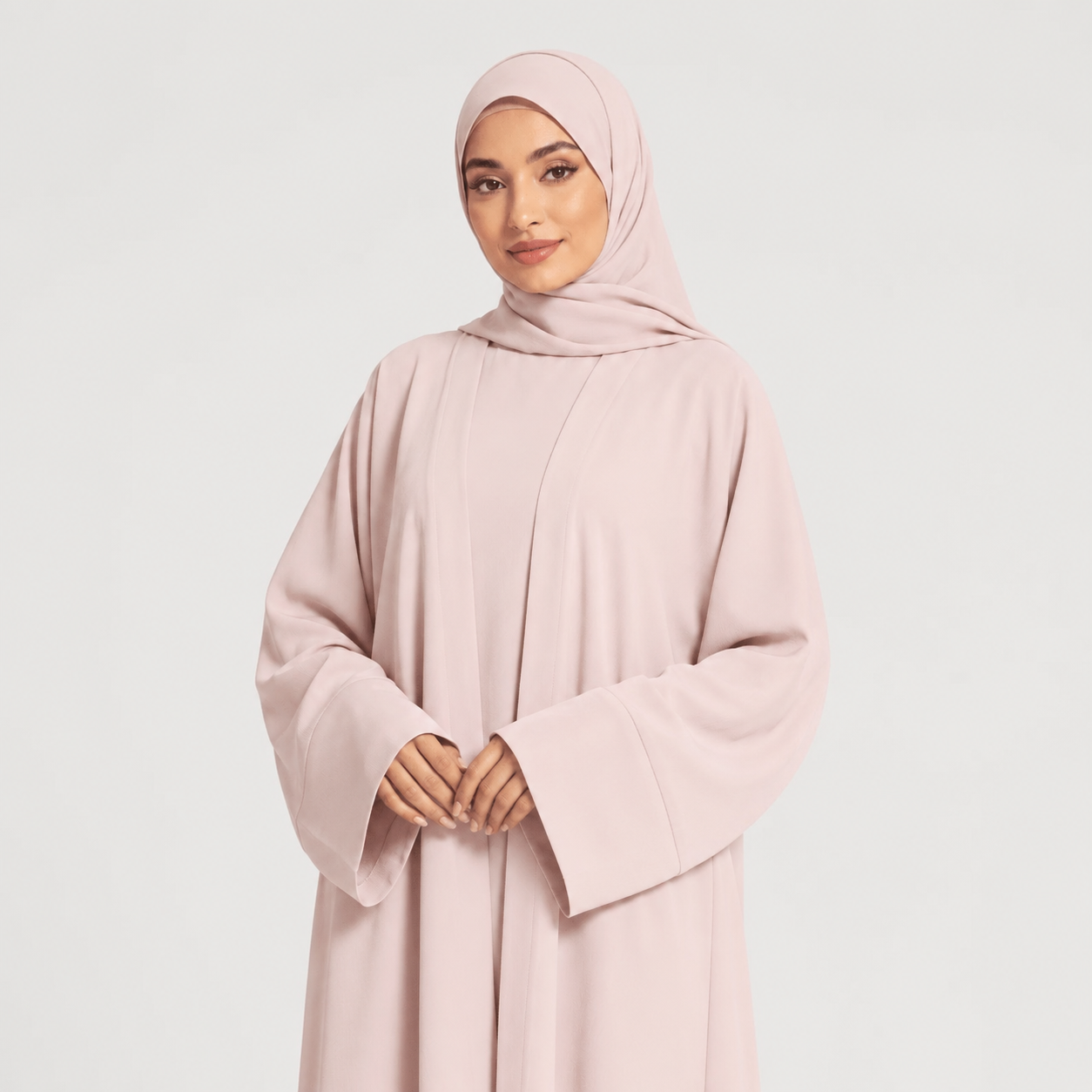 Woman wearing a light pink abaya and hijab on a white background