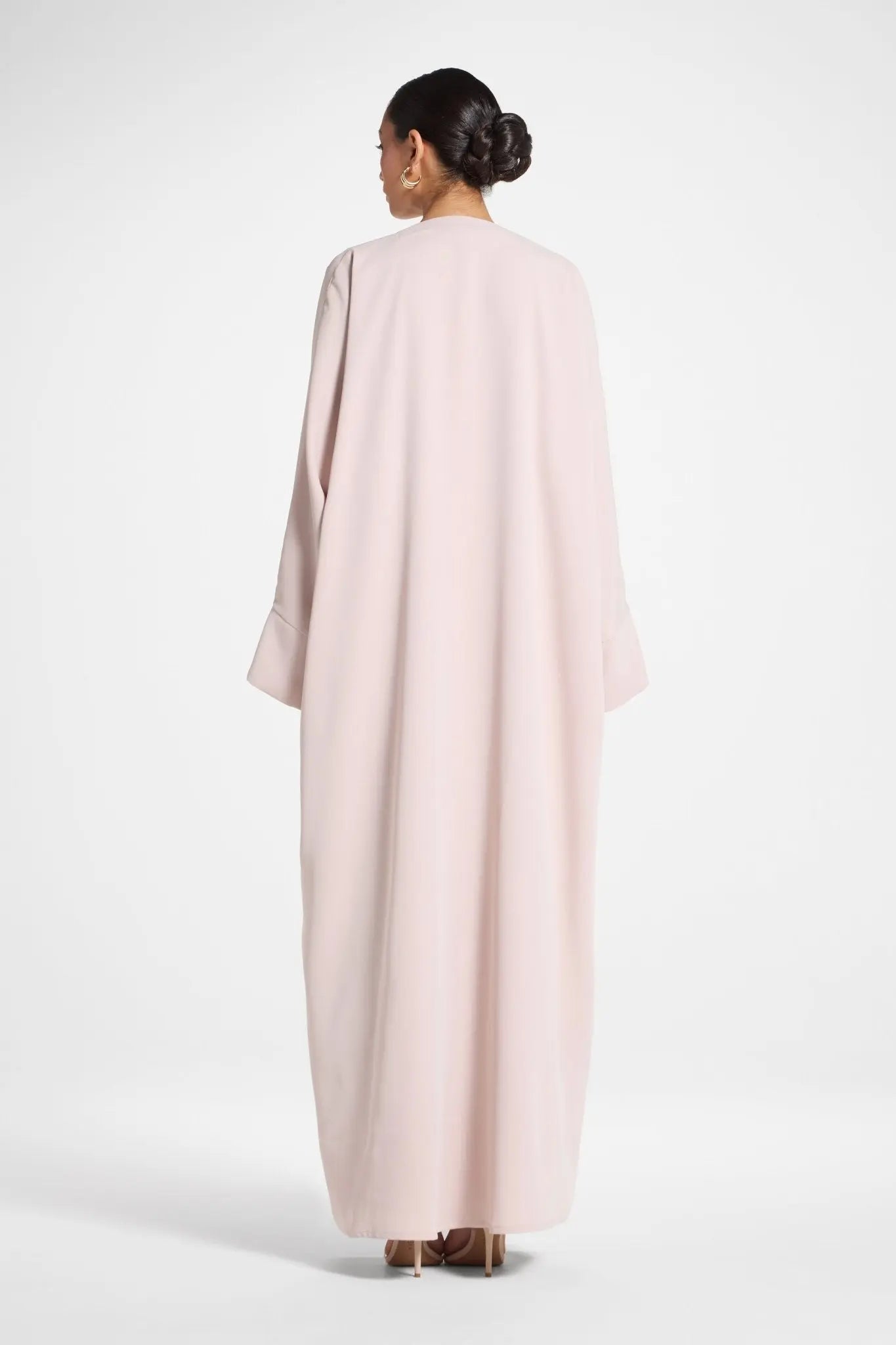 Woman wearing a light pink abaya on a white background