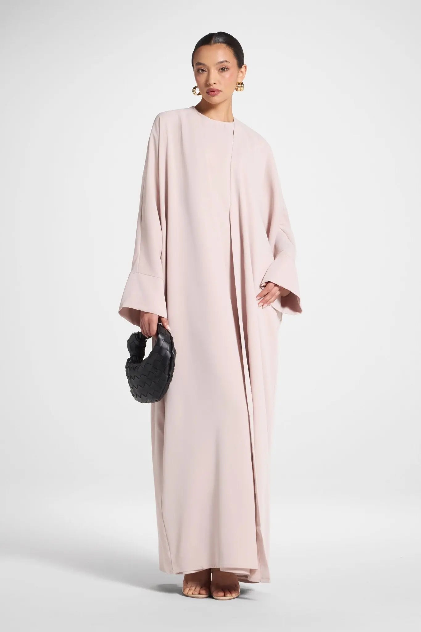 Woman wearing a long, light pink dress holding a black clutch against a white background