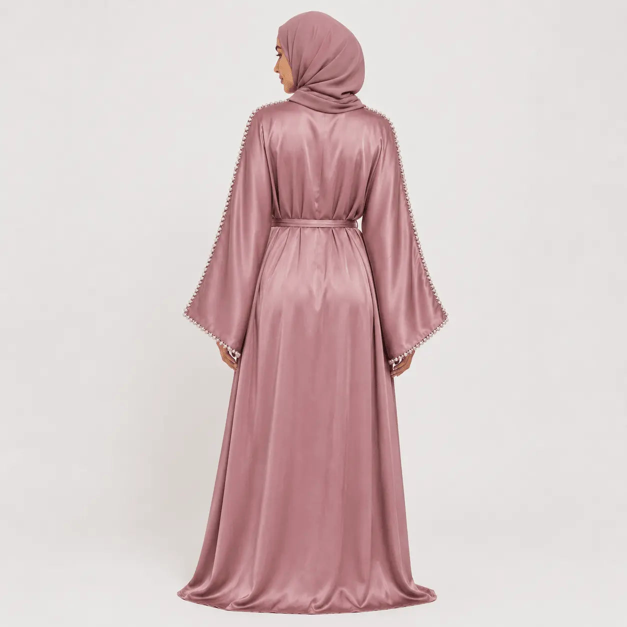 Woman wearing a pink abaya with intricate detailing on a white background