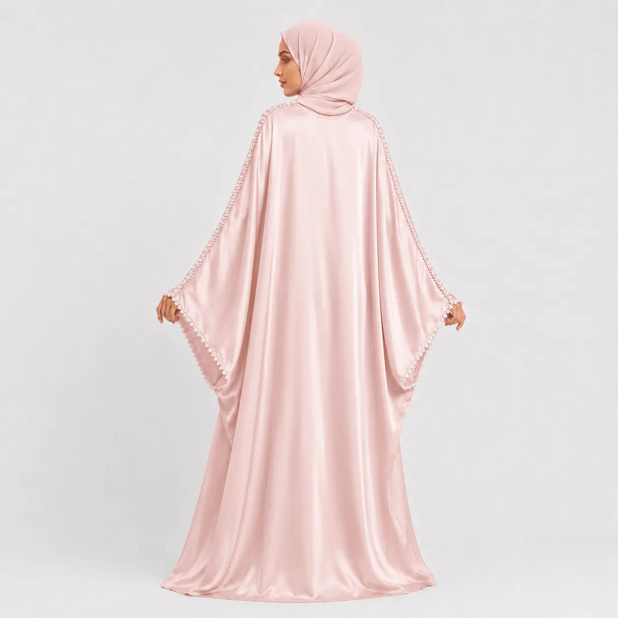 Woman wearing a pink abaya with a matching hijab on a light gray background