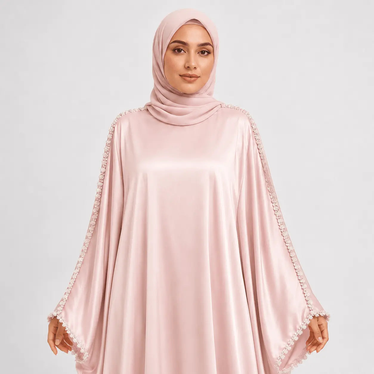 Woman wearing a light pink abaya with lace details on a white background