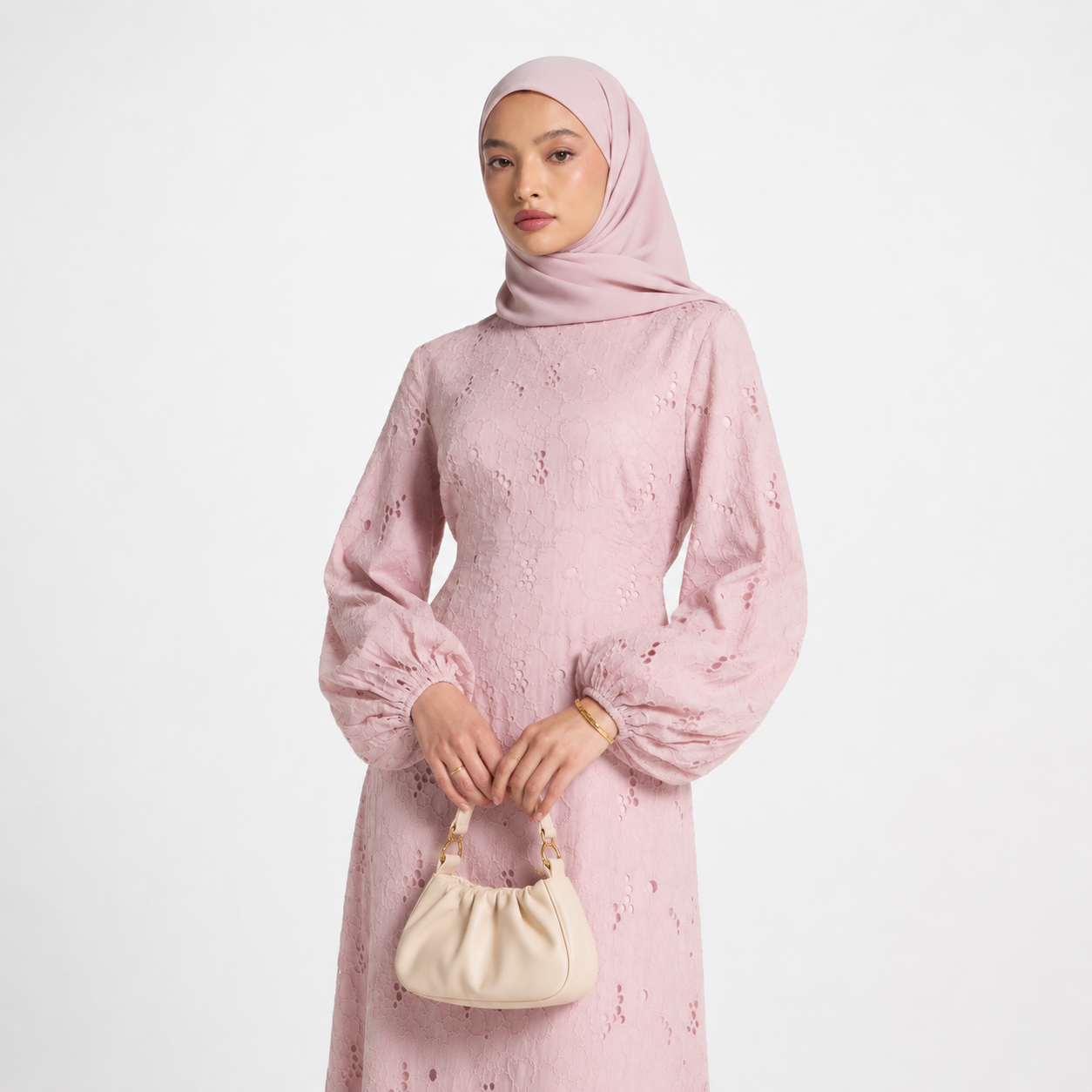 Woman wearing a pink dress and hijab holding a beige handbag on a light gray background