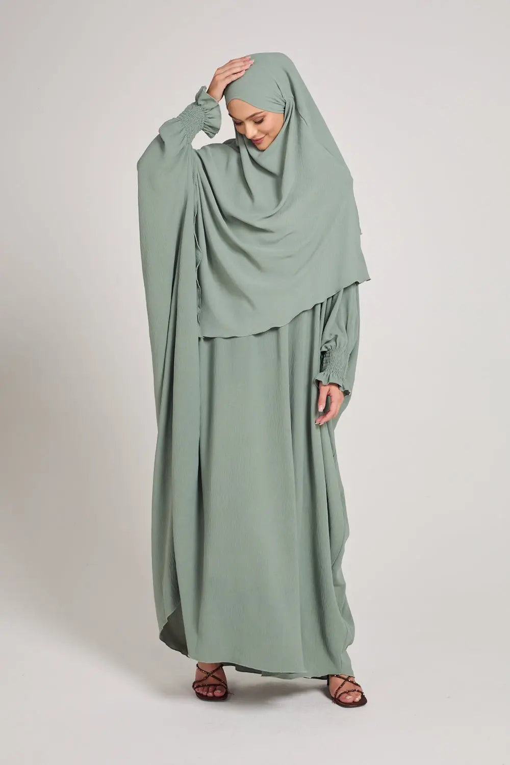 Woman wearing a light green abaya on a white background