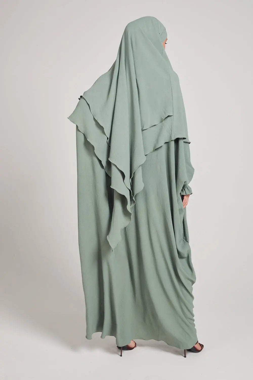 Person wearing a light green abaya with ruffled details on a white background