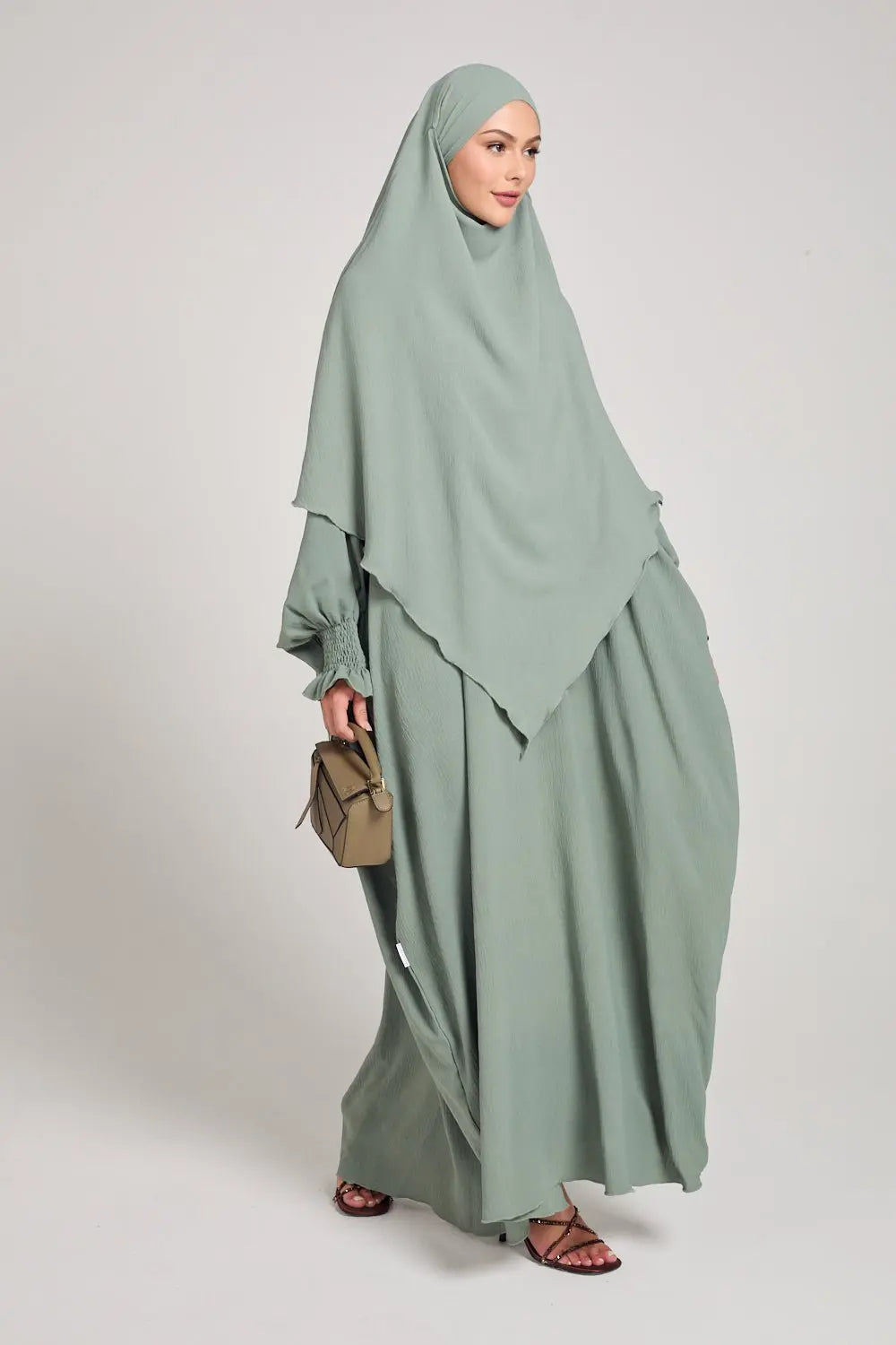 Woman wearing a light green abaya with a matching hijab on a white background