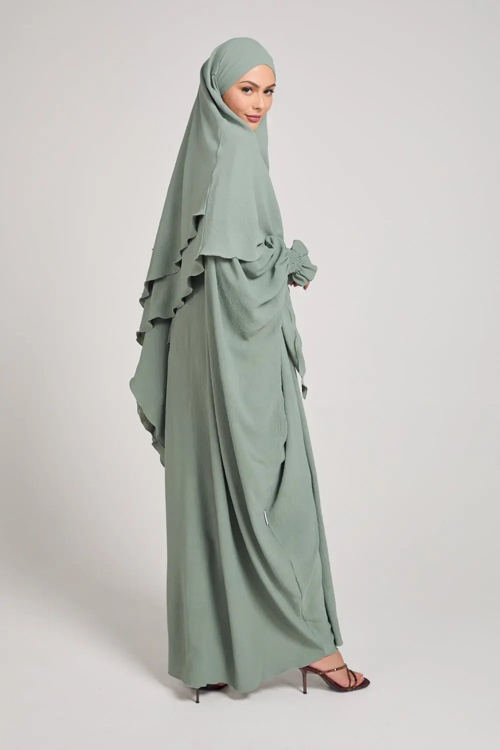 Woman wearing a light green abaya on a plain background