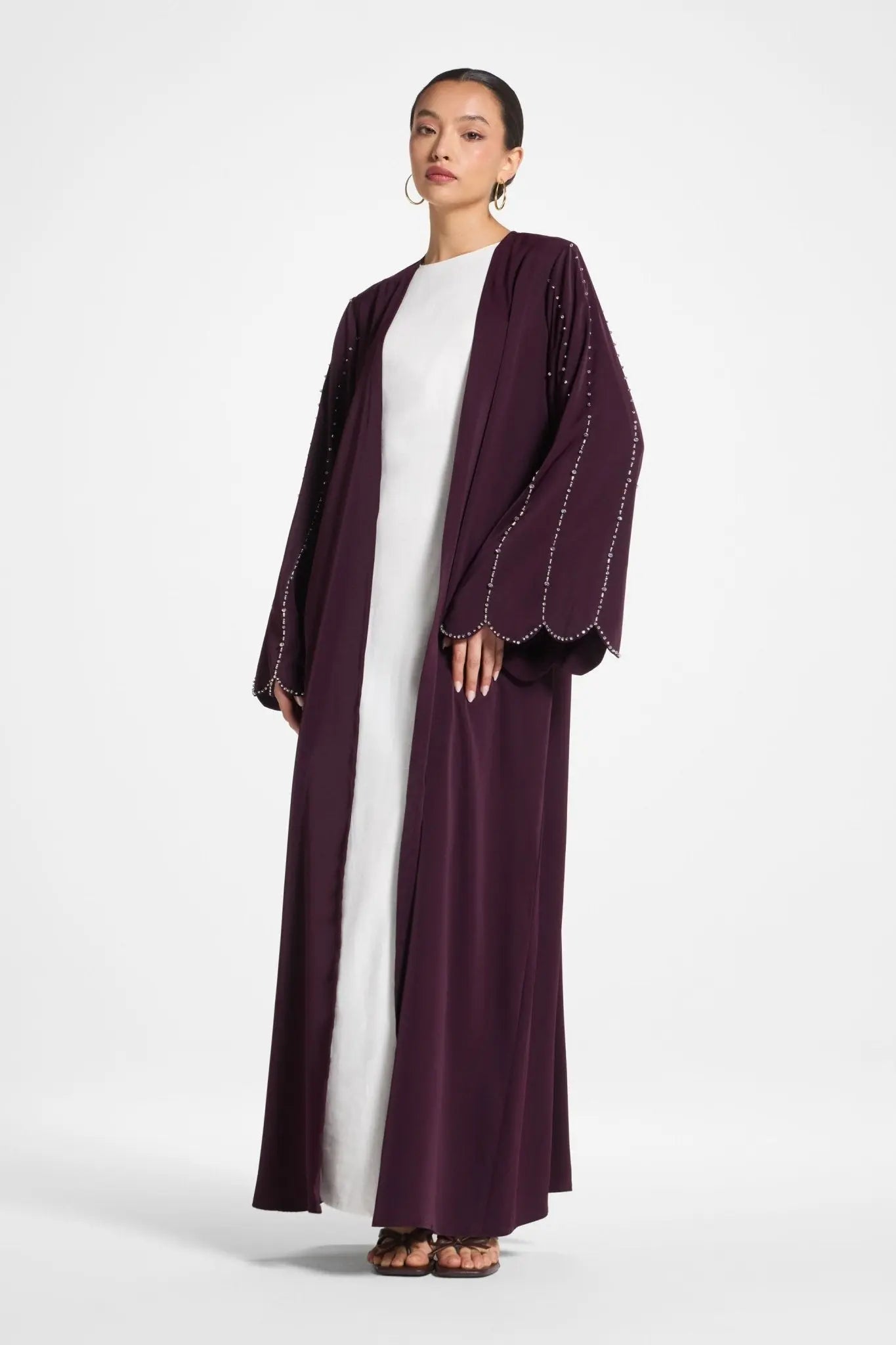 Woman wearing a long, dark purple abaya over a white outfit on a white background