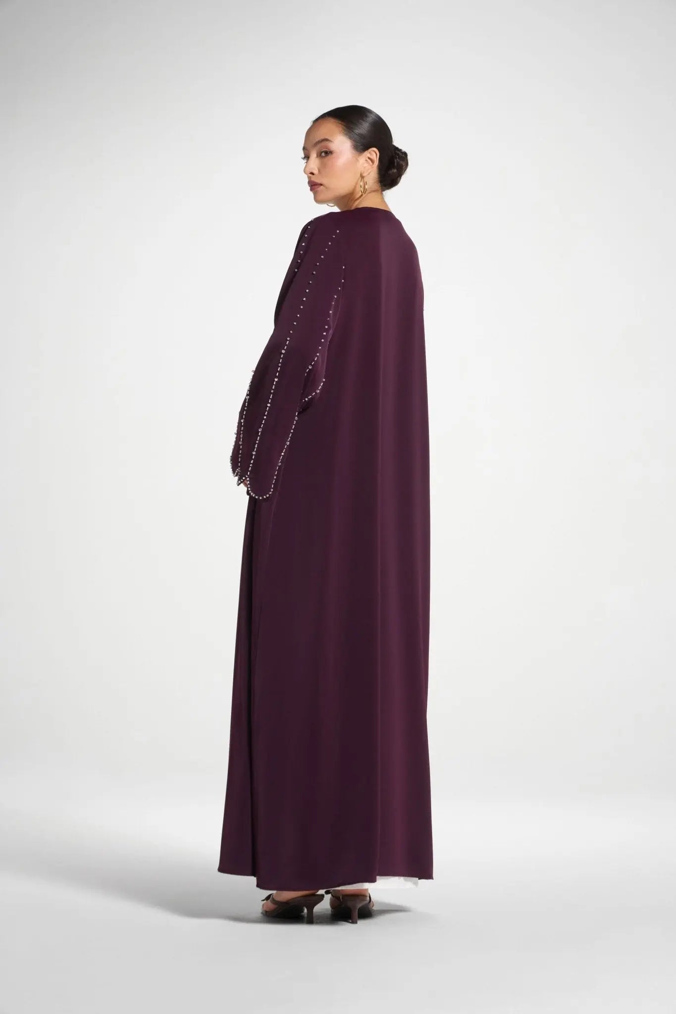 Woman wearing a long burgundy dress with embellishments on a white background