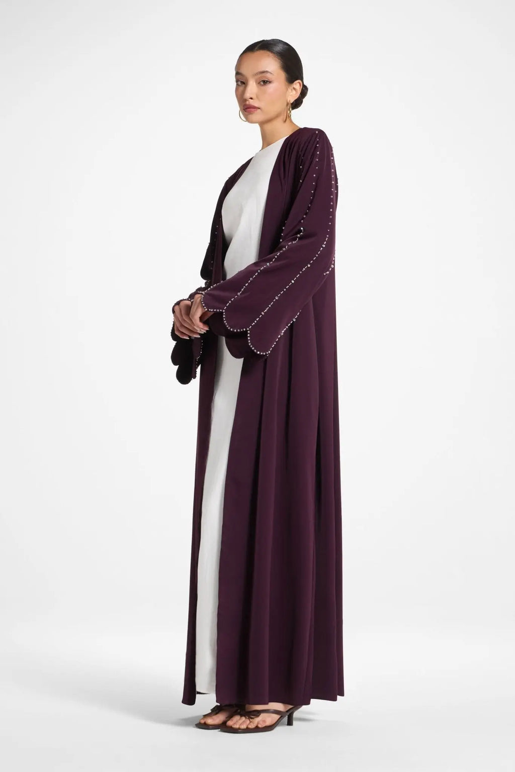 Woman wearing a long, dark purple dress with white accents on a white background