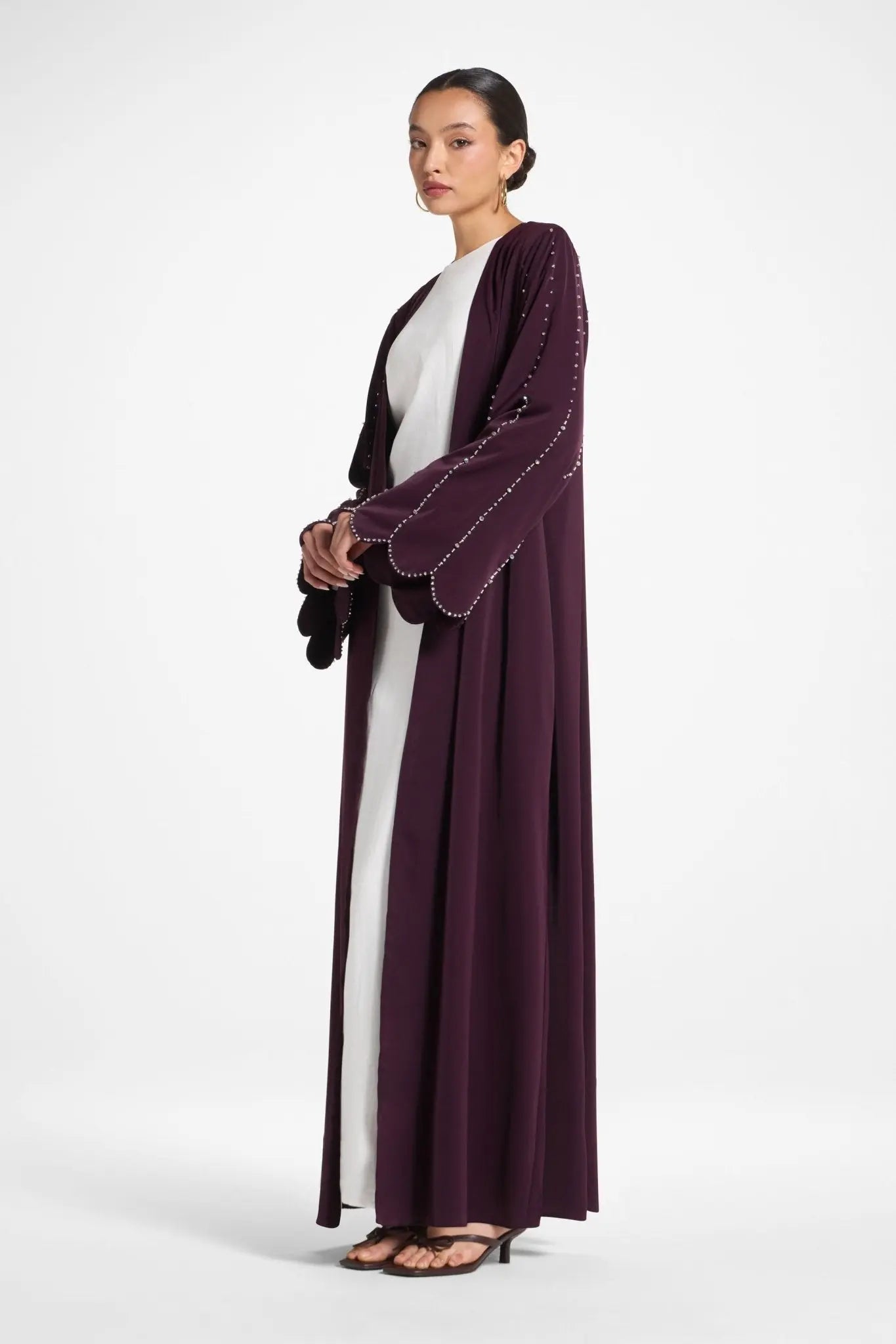Woman wearing a long, dark purple dress with white accents on a white background