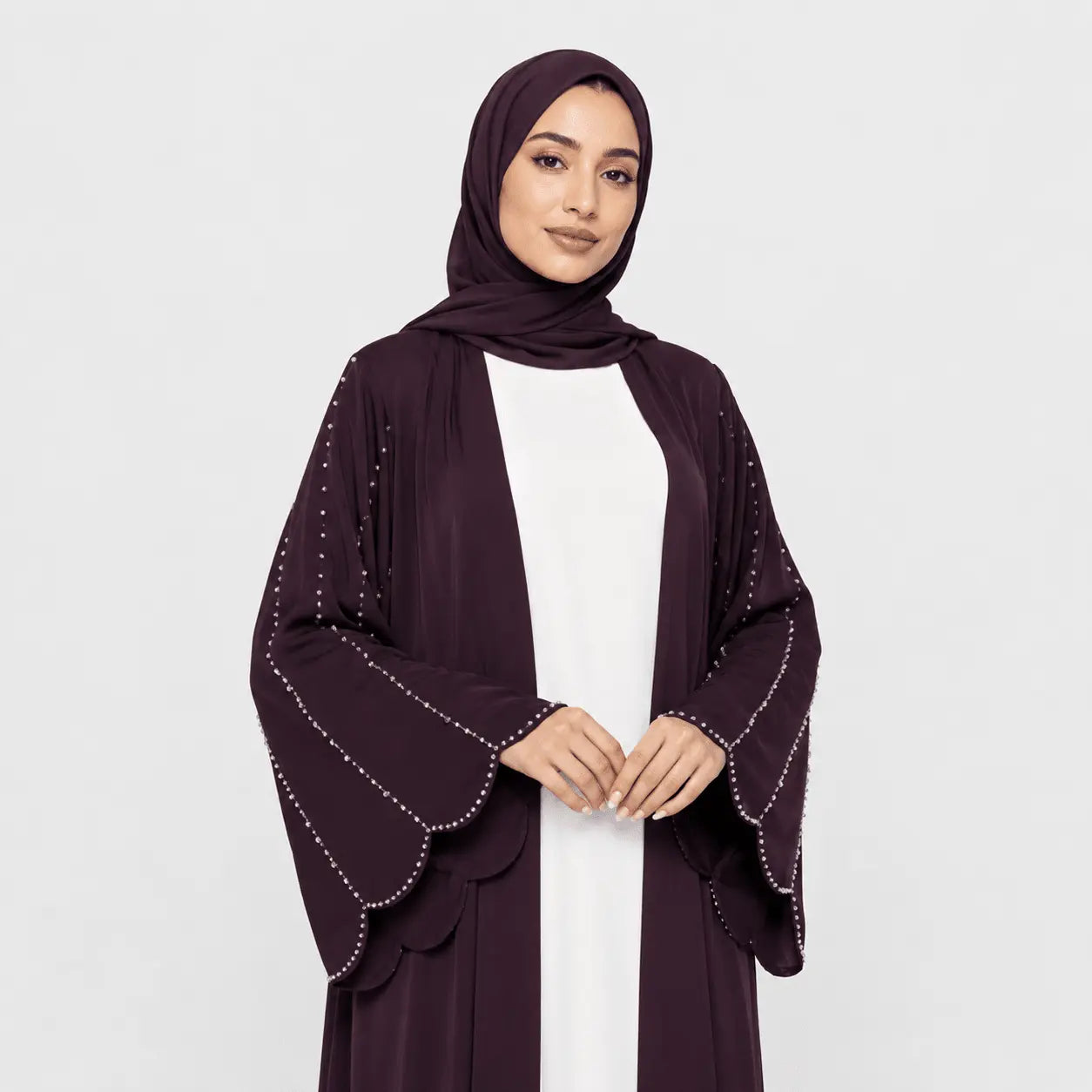 Woman wearing a dark purple abaya with white embellishments on a light gray background