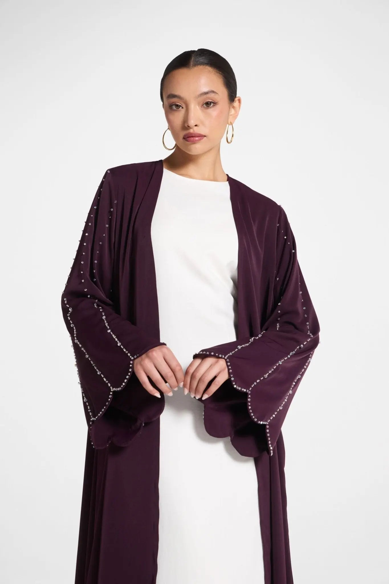 Woman wearing a dark purple embellished cardigan over a white dress on a white background