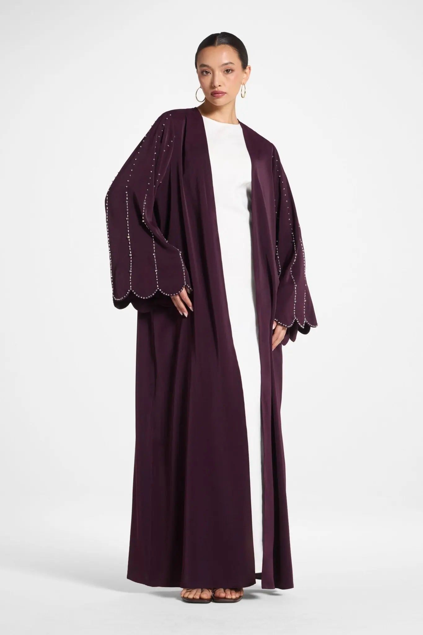 Woman wearing a long, dark purple abaya with white trim on a white background