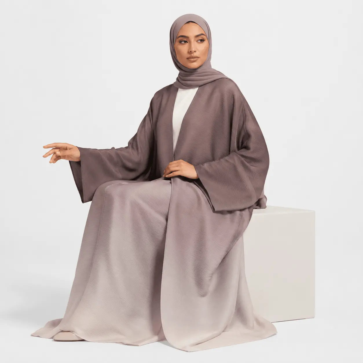 Woman wearing a long, light brown abaya with a matching hijab on a white background
