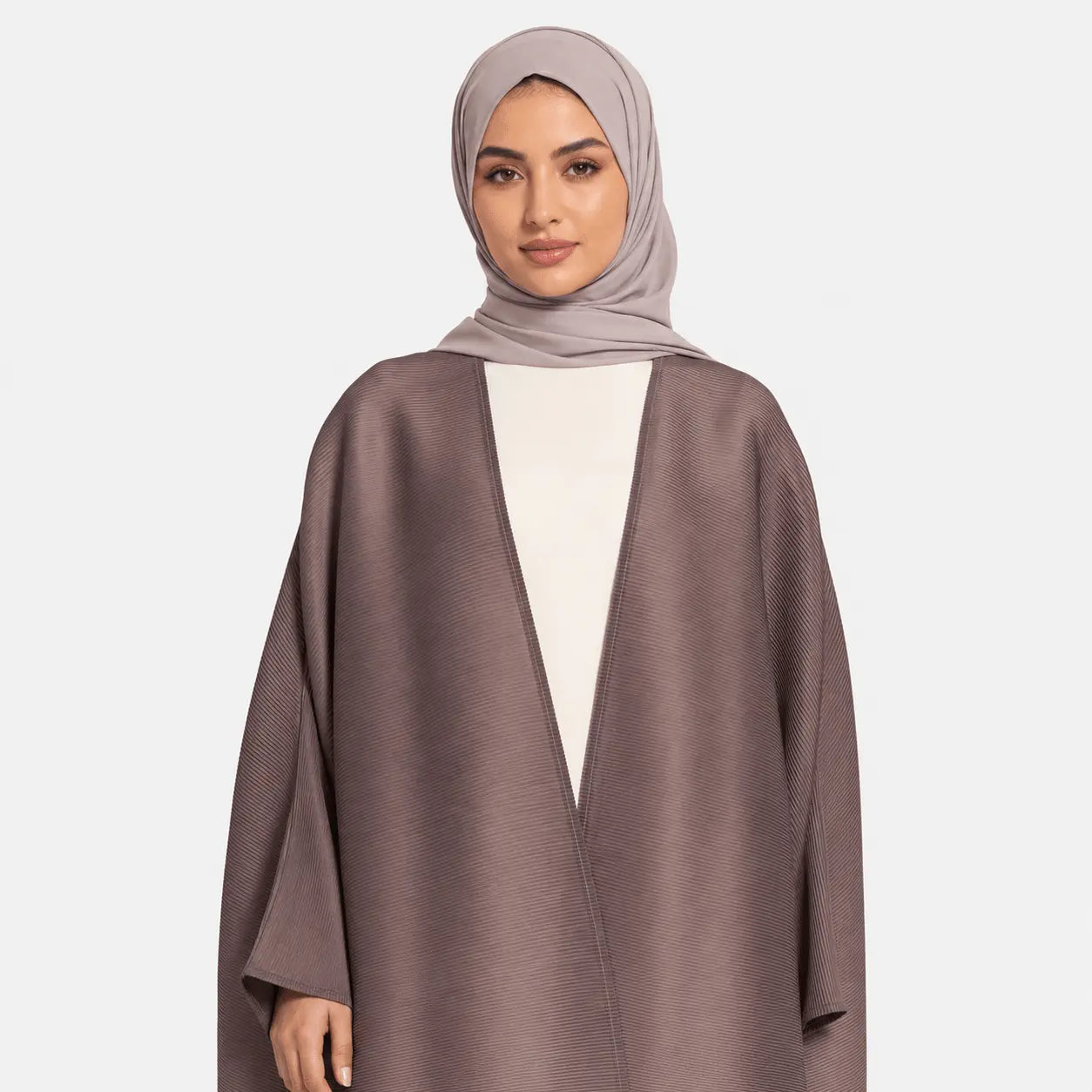 Woman wearing a brown abaya and beige hijab on a white background