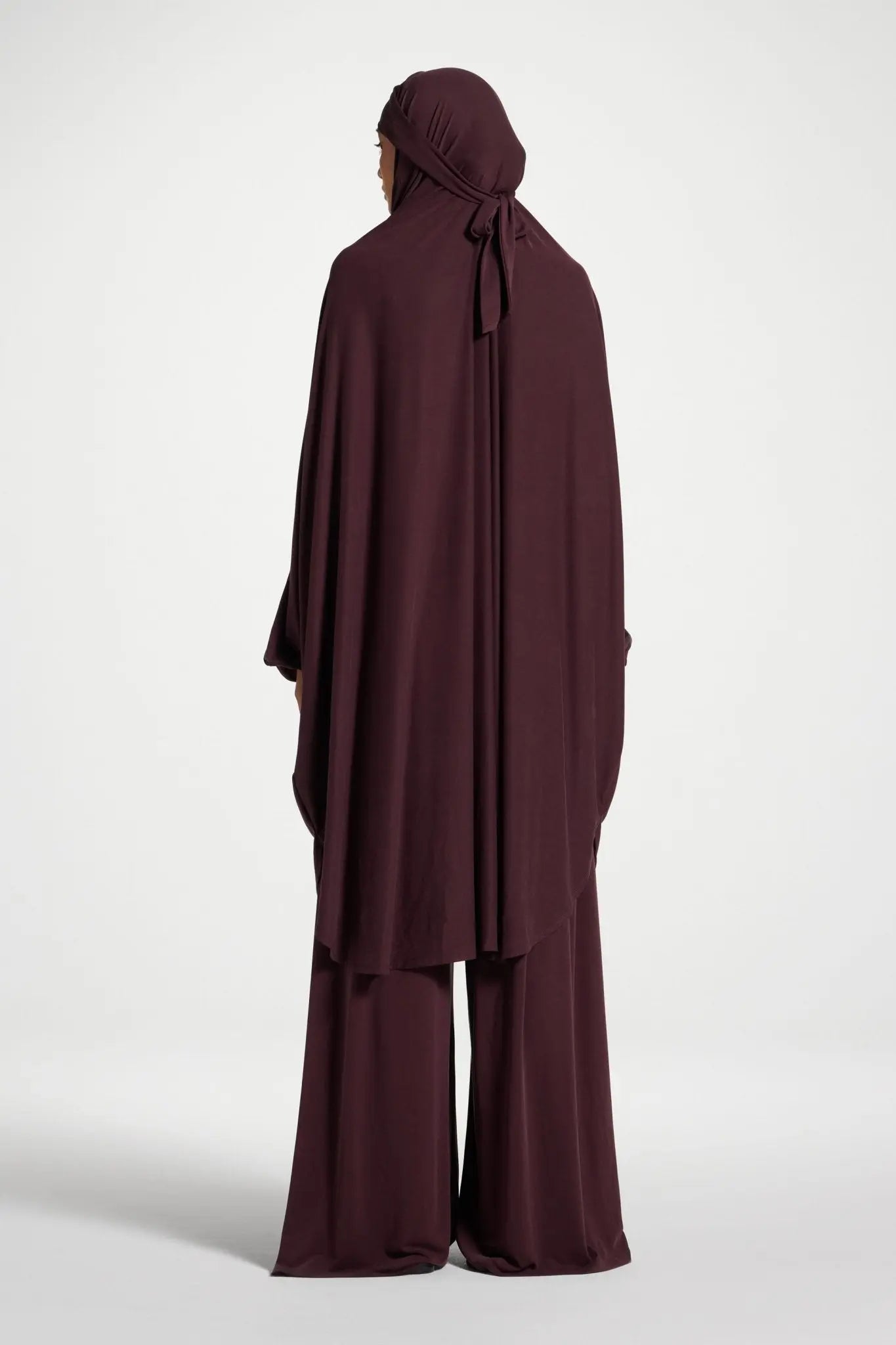 Person wearing a burgundy abaya with a matching hijab on a white background