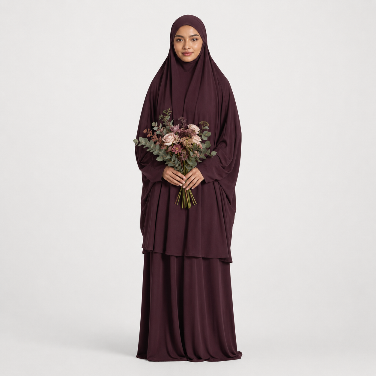 Woman in a burgundy abaya holding a bouquet of flowers on a light gray background