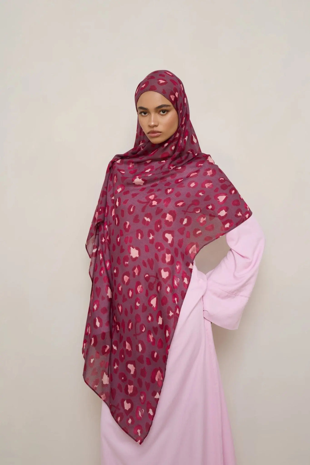 Woman wearing a patterned hijab and pink outfit against a plain background