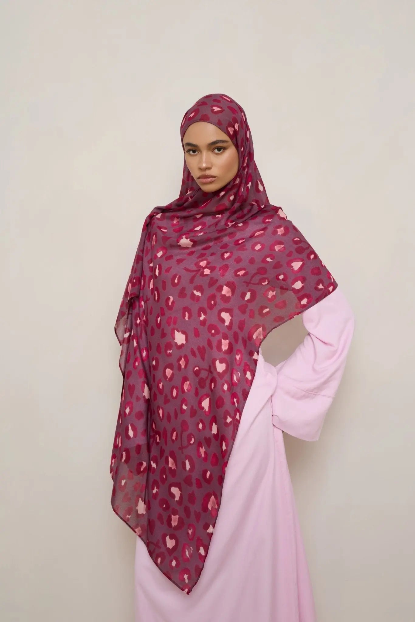 Woman wearing a patterned hijab and pink outfit against a plain background