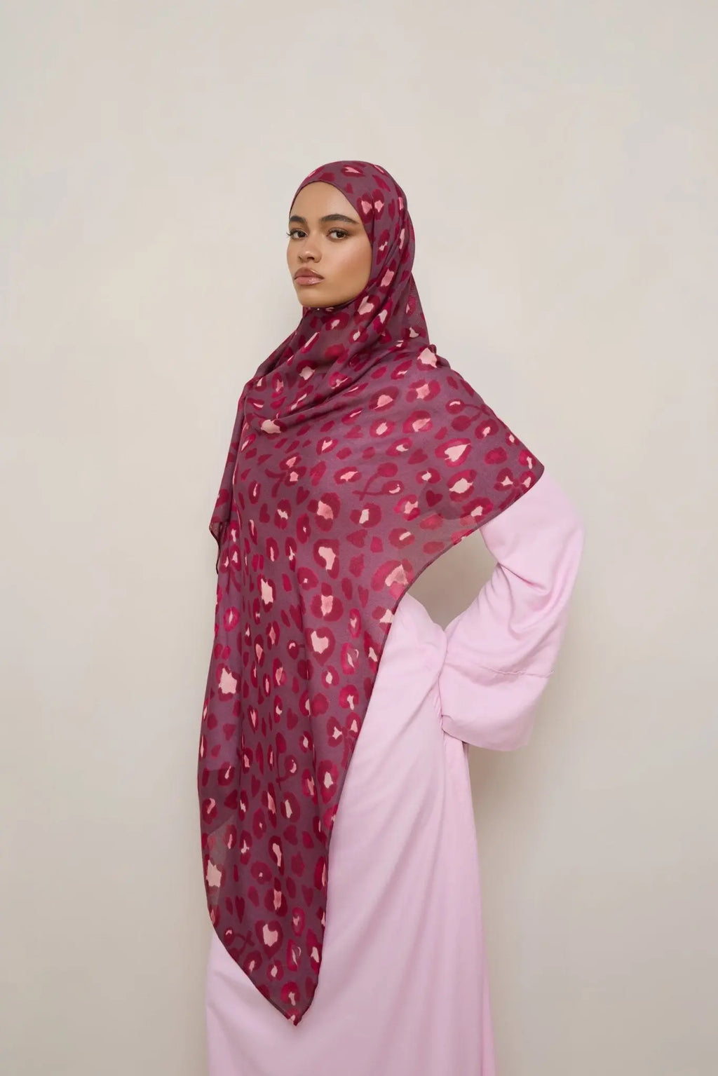 Woman wearing a patterned hijab and pink outfit against a plain background