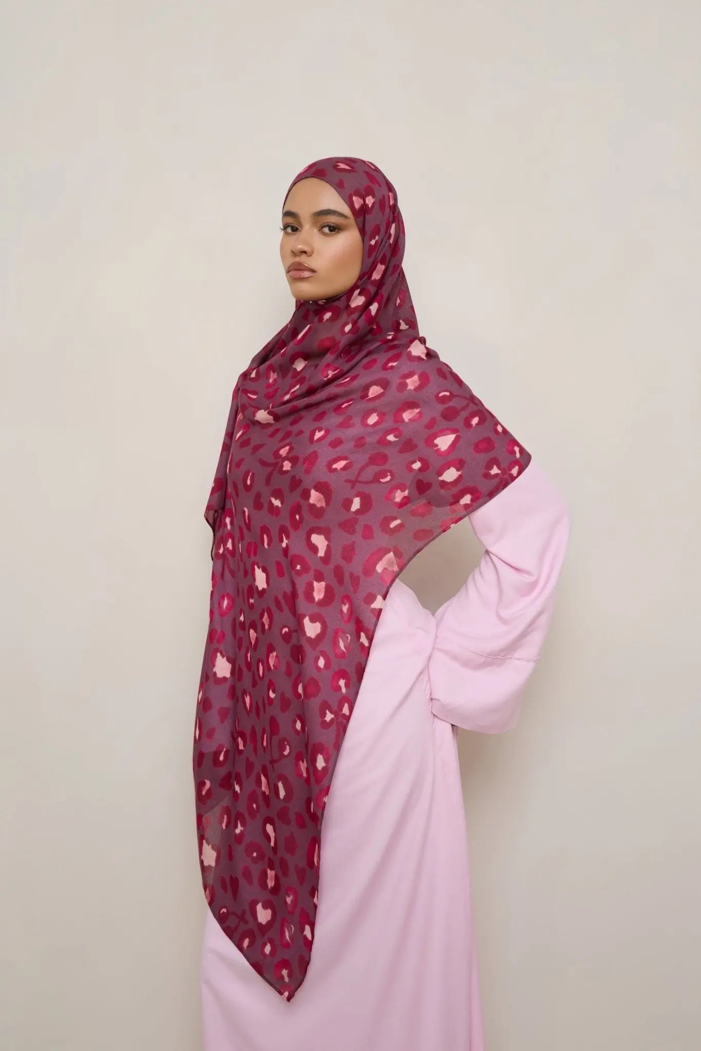 Woman wearing a patterned hijab and pink outfit against a plain background