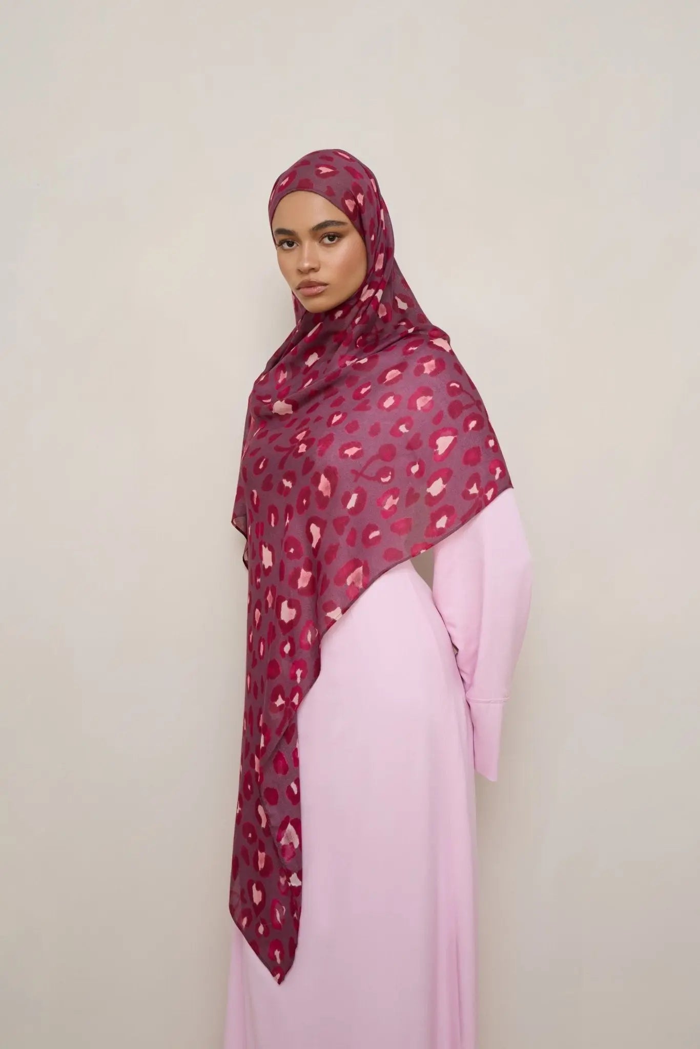 Woman wearing a patterned hijab and pink dress against a plain background