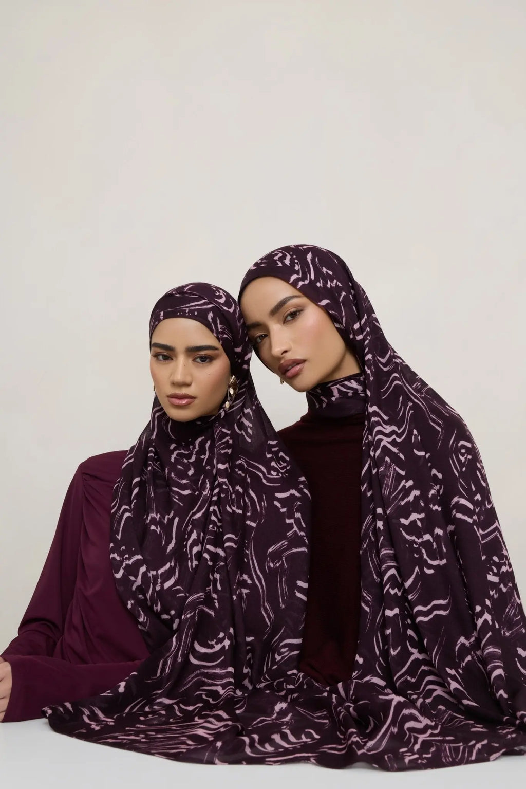 Two women wearing matching purple hijabs with a pattern against a white background