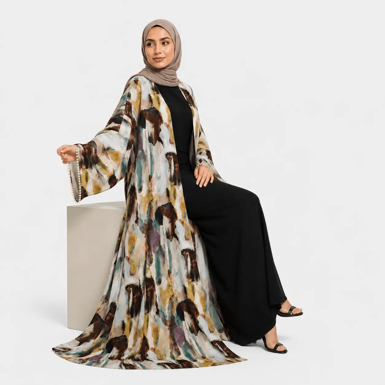 Woman wearing a patterned abaya and hijab on a white background