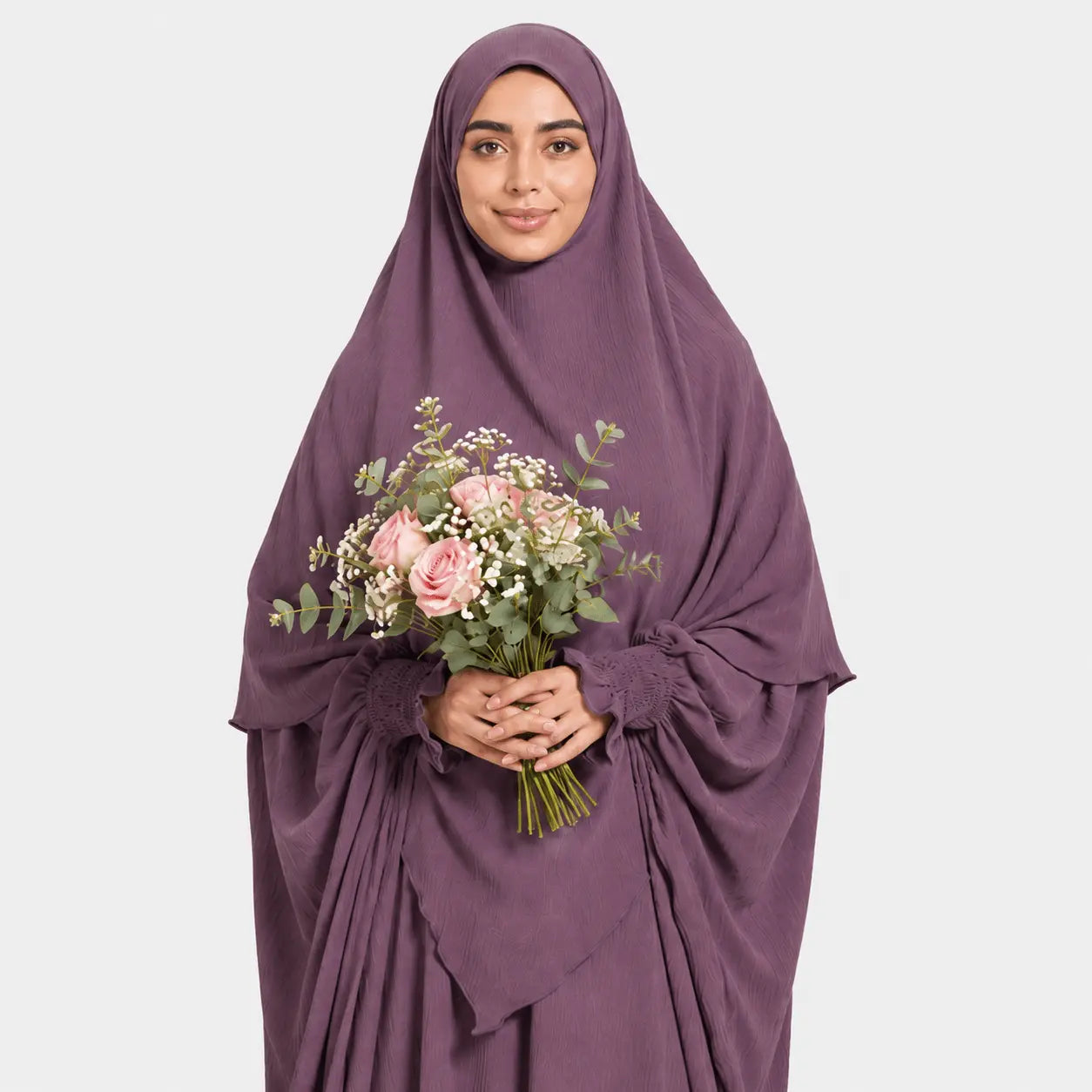 Woman wearing a purple hijab and holding a bouquet of flowers on a light gray background