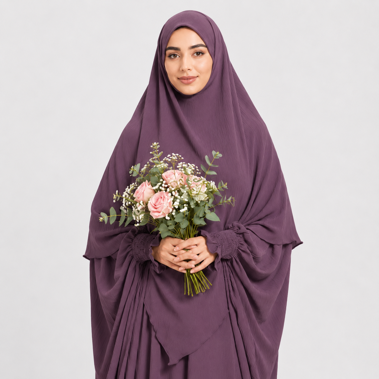 Woman wearing a purple hijab and holding a bouquet of flowers on a light gray background