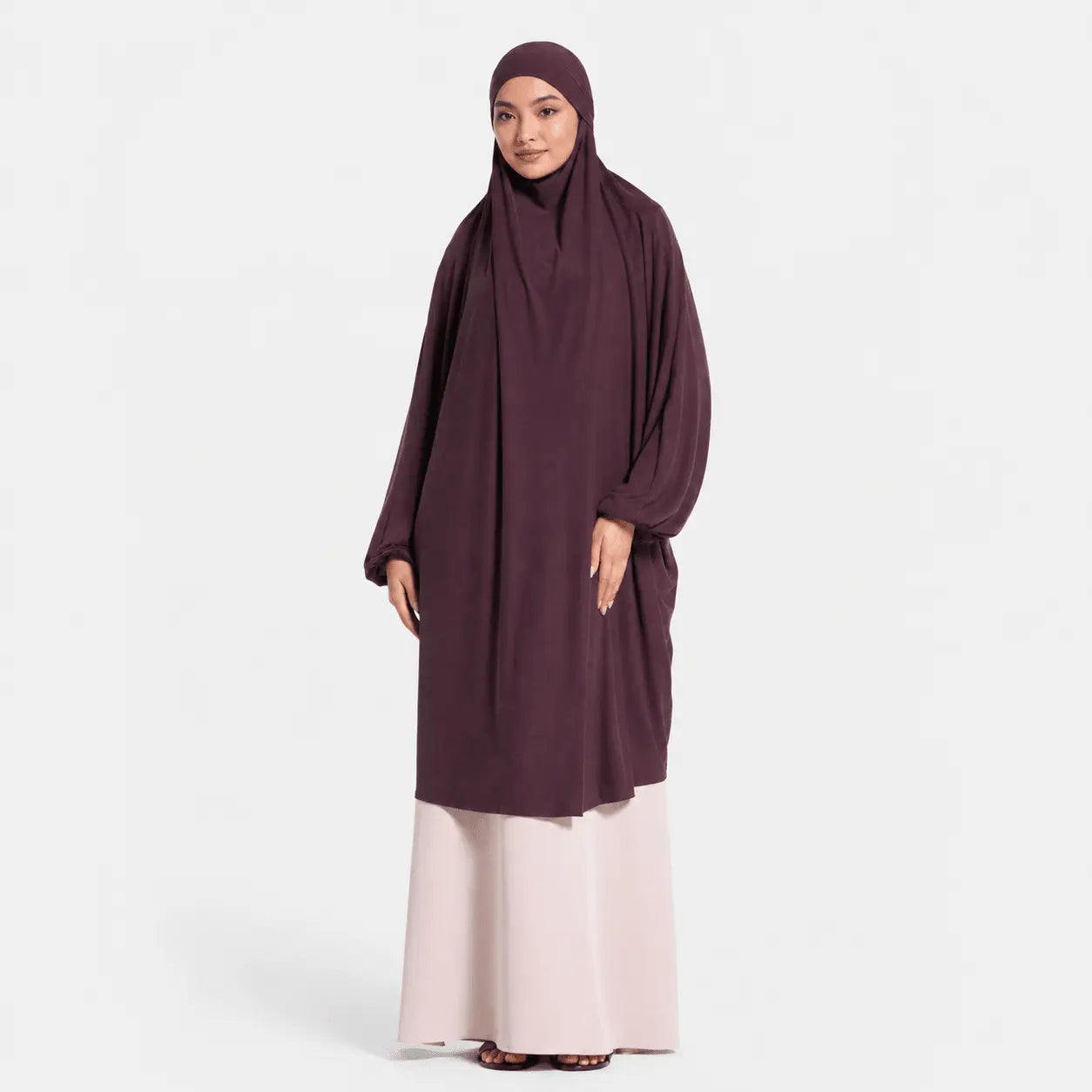 Woman wearing a dark purple abaya with a white skirt on a light gray background
