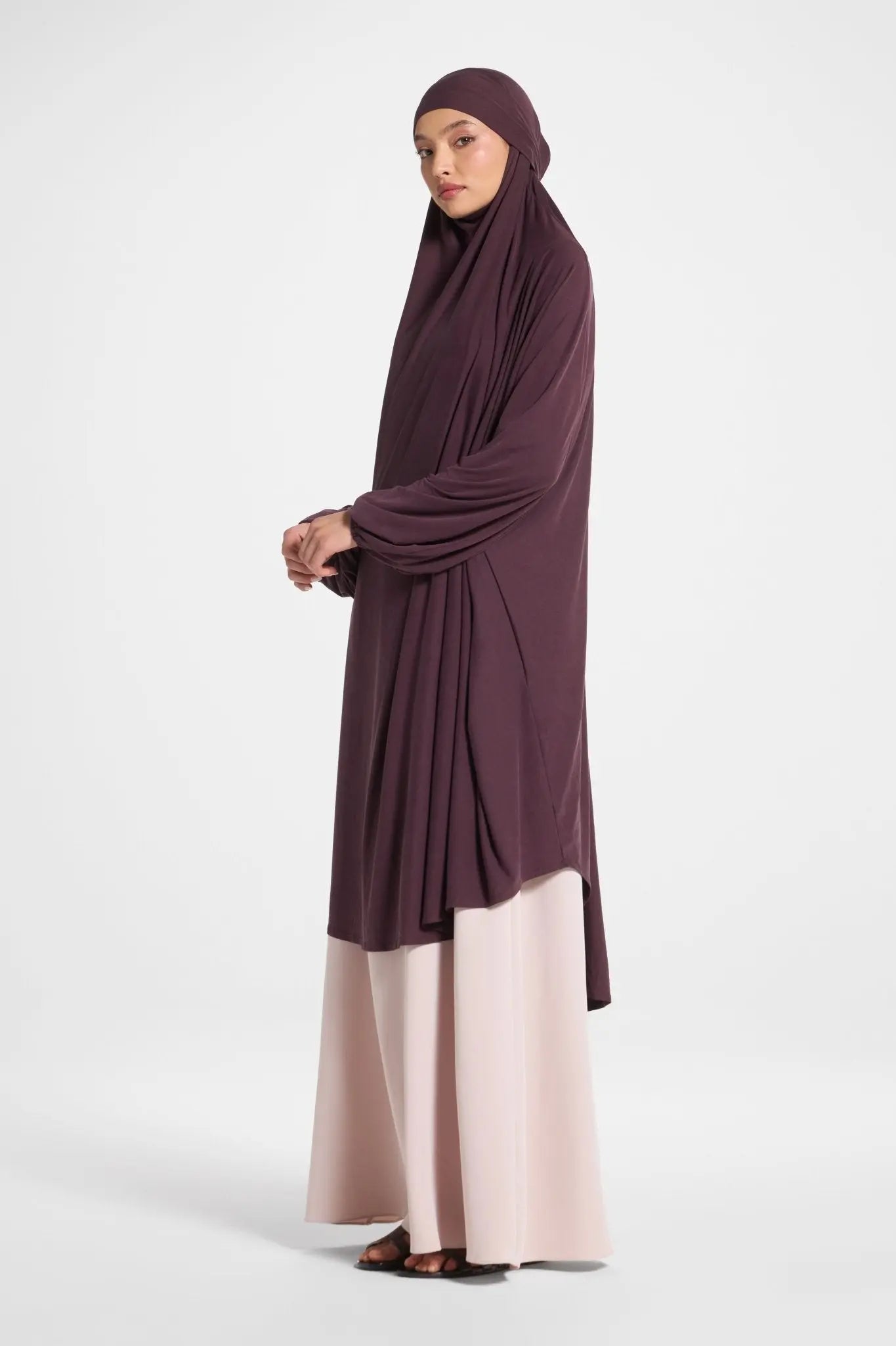 Woman wearing a dark purple hijab and beige pants on a white background