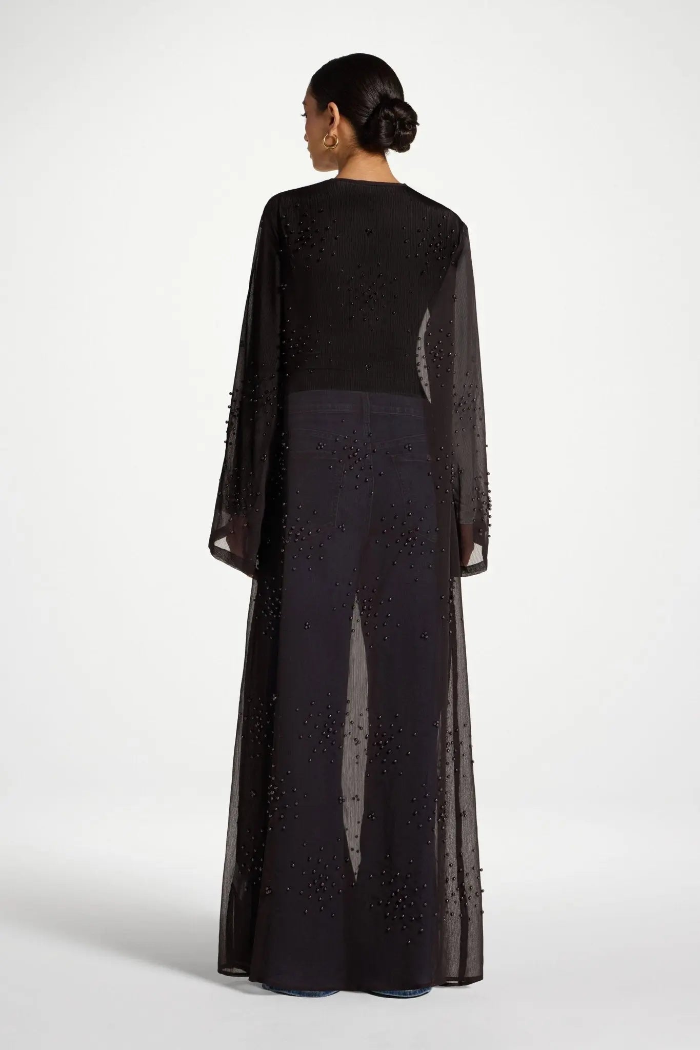 Woman wearing a black outfit with sheer sleeves on a white background