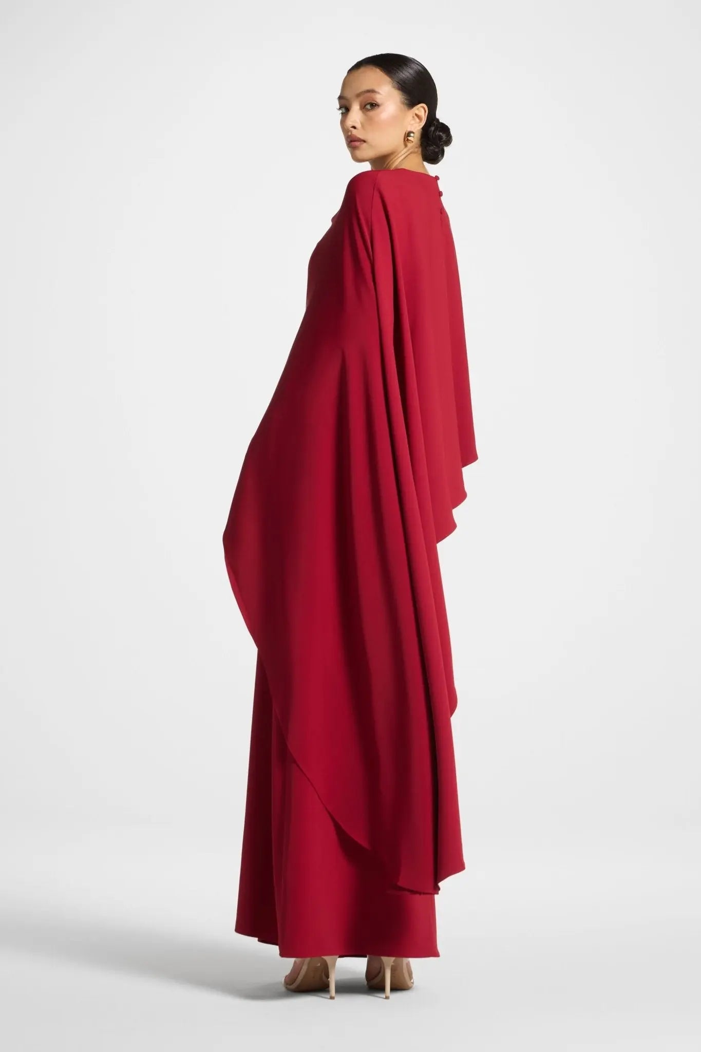 Woman wearing a red dress with a cape-like design on a white background